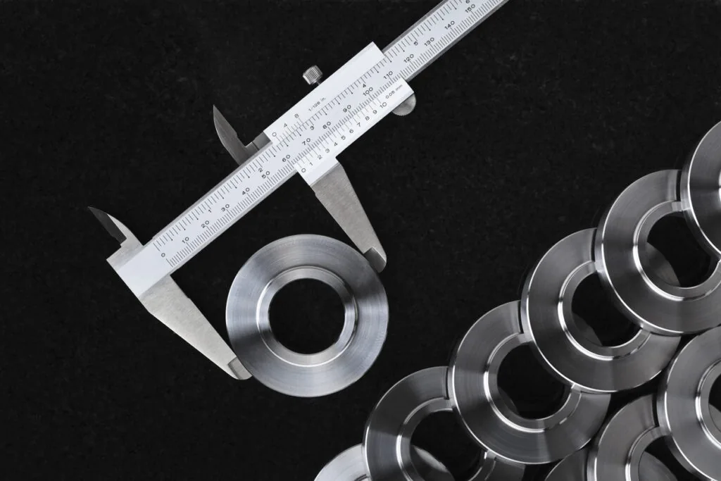 Digital micrometer measuring a precision CNC machined part alongside others machined parts measuring the CNC milling tolerances of the parts.