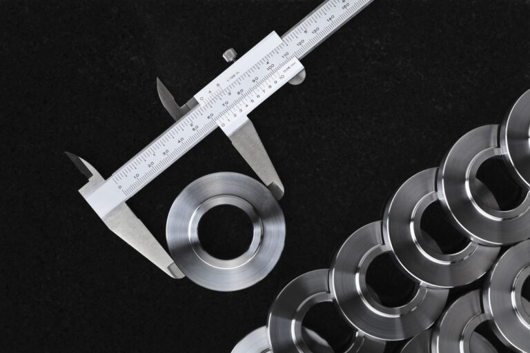 Digital micrometer measuring a precision CNC machined part alongside others machined parts measuring the CNC milling tolerances of the parts.
