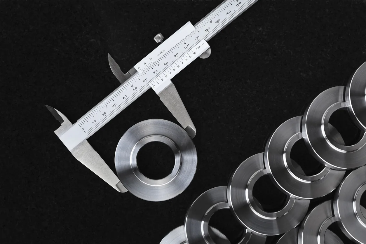Digital micrometer measuring a precision CNC machined part alongside others machined parts measuring the CNC milling tolerances of the parts.